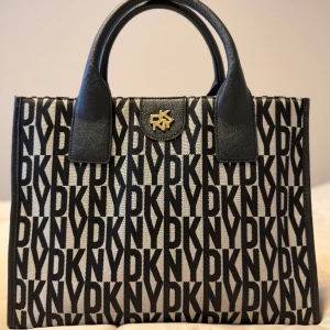 DKNY CAROL BOOK TOTE - Tote bag - DKNY CAROL BOOK TOTE - Tote bag (Ny) Dustbag samt axelband medföljer.   Height: 26 cm  Length: 33 cm  Width: 16 cm  Carrying handle: 12 cm    Nypris: 3000 kr