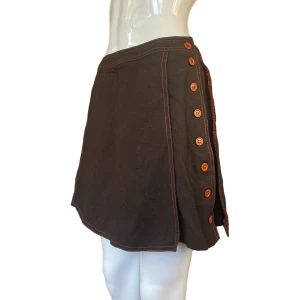 Skort - En äldre skort i fint skick! Ger 70tals känsla. Storlek 42. Tror den är liten i storlek, KOLLA GÄRNA MÅTTEN INNAN KÖP! Brunt material med orangea sömmar. Ser ut som en kjol när man bär den, men finns shorts under. Midjebredd 35cm & längd 40cm