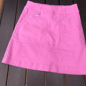 Golfkjol Daily Sports st 34 - Golfkjol Daily Sports storlek 34  Markeringsknapp fram på golfkjolen.  Strechtyg med innerbyxa.  Längd 43 cm  Endast provad, fått den som present.  Ljuvlig färg lavendelrosa. 
