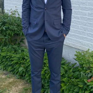 Kostym kavaj stl 50 byxa stl 52 marinblå - Kostym endast använd 2 ggr, köpt på H&M vår-23, mycket fint skick. Marinblå. Slim fit. Byxa stl 52 skinny fit. Kavaj stl 50 slim fit, obs näsduk ingår ej. Skjorta stl S easy iron. Nypris ca 1550kr
