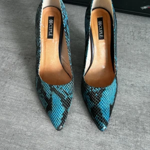 Pumps från Couple - Pumps från Couple i svartblått ormskinnsmönster och röd sula. Lite använda så inte nötta. Storlek 38. Tillverkade i Spanien, köpta i Malaga.