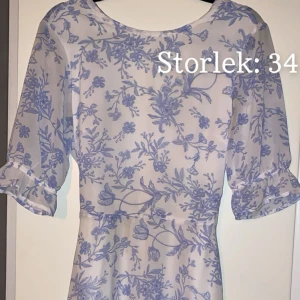 Sommarklänning  - Knälång vit klänning med ljusblåa blommor i olika motiv. Har en tunn dragkedja på ryggen. Använd några gånger, inga hål eller fläckar och är inte urtvättad.   Exl. Frakt 