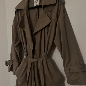 Lång trenchcoat Zara - Säljer min långa trenchcoat från Zara eftersom den är för liten för mig. Jackan sitter lite oversized, den har två framfickor, dubbelknäppning fram med knappar och en öppning där bak som går att knäppa till. Perfekt till vår och höst🍂🌼 Använt 2-3ggr!