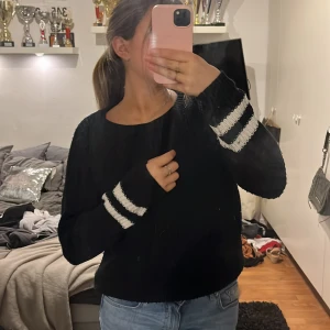 Svart stickad - Mycket fin stilren stickad tröja med två vita ränder på vardera arm. Passar perfekt en sen sommar kväll eller en vinter förmiddag till ett par jeans