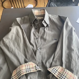 Burberry skjorta - Säljer nu en sjukt fet Burberry skjorta i 10/10 skick. Färgen är en sällsynt och snygg grå/grön färg. Nypris är runt 4000-5000kr🍾 Skriv vid frågor!