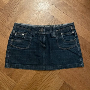 Mini jeanskjol - Lågmidjad minikjol denim! Köpt second hand, använd 2-3 gånger av mig! Storlek 38 Saknas en svart sten på höger bakficka (bild 3), men är utöver det i bra skick!  Midjemått rakt över: 42 cm Längd totalt: 32 cm