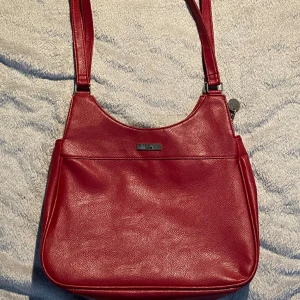 vinröd väska i fakeläder - väskan är i bra skick även fast den ä gammal, Vet inte riktigt om de är något bra märke då jag inte vet mycket alls om väskor. Det är ett litet fack på baksidan och två små inuti utöver det stora 💌