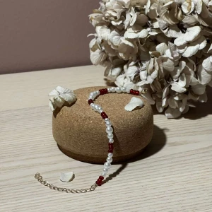 Armband - Ilona - Detta armband är gjort av vita pärlor i tre olika storlekar som skapar ett vackert mönster. Till de vita pärlorna har vi valt våra röda fina glaspärlor. Detta armband har även en kedja i guldplätering.  Namn: Ilona Längd: Hela 24 cm, Pärlor 15,5 cm 