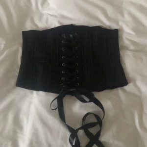 Kritstrecksrandigt underkorsett strl M - Korsett som sitter under byst, i perfekt skick. Äkta korsett, med boning. Längd: 37-40cm. Midja som den är snörad nu: 41cm x2. Som snävast: 39cm x2. Kan passa större storlekar vid justering av snöre. Finns inga bilder på. Köparen står för frakt.