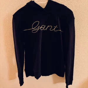 Hoodie Gant - Mörkblå junior gant script hoodie i nyskick, knappt använd, skick 10/10 inga märken eller hål. Öppen till förhandling . Texten är guldig