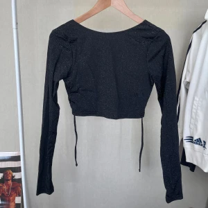 Topp med öppen rygg - En svartglittrig topp med öppen rygg o lite croppad, storlek S från nakd! Knappt använd! Perfekt som en festtopp! Kontakta för fler frågor!💛💛