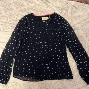 Snygg blus med små snöflingor  - En supersnygg mörkblå blus med vita snöflingor, halvt genomskinliga puffärmar och volanger framtill, nästintill oanvänd ✨