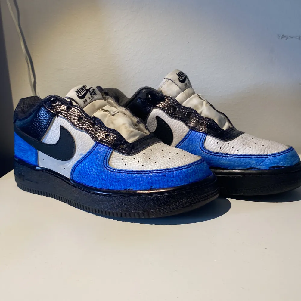 hej! jag säljer ett par Nike Air Force 1 sneakers i blått, svart och vit de är i helt okej skicka alla slitage är med på bild. de är målade av mig och där av säljs biligt. hör av er vid minsta sak!!. Skor.