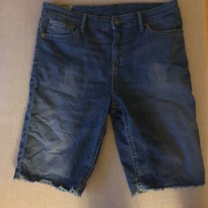 Blå jeansshorts från Polo Ralph Lauren - Ett par blå jeansshorts från Polo Ralph Lauren. Shortsen har en klassisk femficksdesign och råa kanter vid bensluten. De är tillverkade av denim och har en knapp- och dragkedjestängning framtill. Det är en storlek 8 som motsvarar storlek M i Dam