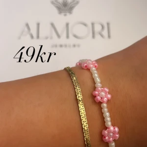 Armband från Almori - Ett vackert armband från Almori. Armbandet består av små vita pärlor och rosa blommor. Perfekt för att ge en elegant touch till din outfit.