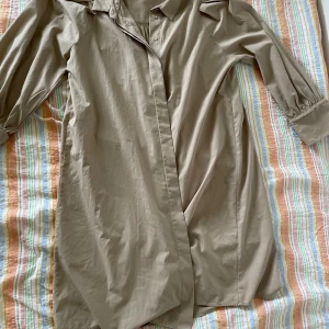 Beige klänning från Fransa - En beige klänning från Fransa i storlek XL. Klänningen har långa ärmar med knappar vid ärmsluten och en klassisk krage. Den har en lös passform och är knälång.