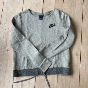 Nike tröja - Niketröja som går att dra ihop nertill eller bara ha som en snygg detalj, är fickor på båda sidor nertill och även en ficka med dragkedja på en ärmen!