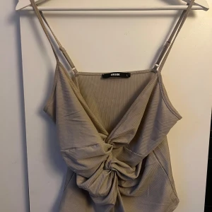 Beige linne från BikBok - Ett beige linne från BikBok med justerbara axelband och en knutdetalj framtill. Linnet har en ribbad textur och är ärmlöst.
