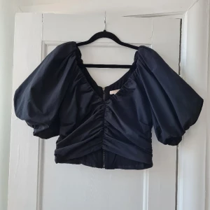 Topp - Svart topp med dragkedja längs hela ryggen och som har stora puffiga ärmar! Aldrig använd! Från H&M. 