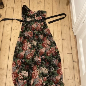 Blommig festklänning med asymetrisk body - Den här är ett riktigt vintagefynd och jag sörjer att den inte passar mig längre! Lång, svart klänning med underbara blomdekorationer. Knytliv under brystet. Asymetrisk över brystet, med en bar axel. Svart underklänning och mönstray meshtyg. 