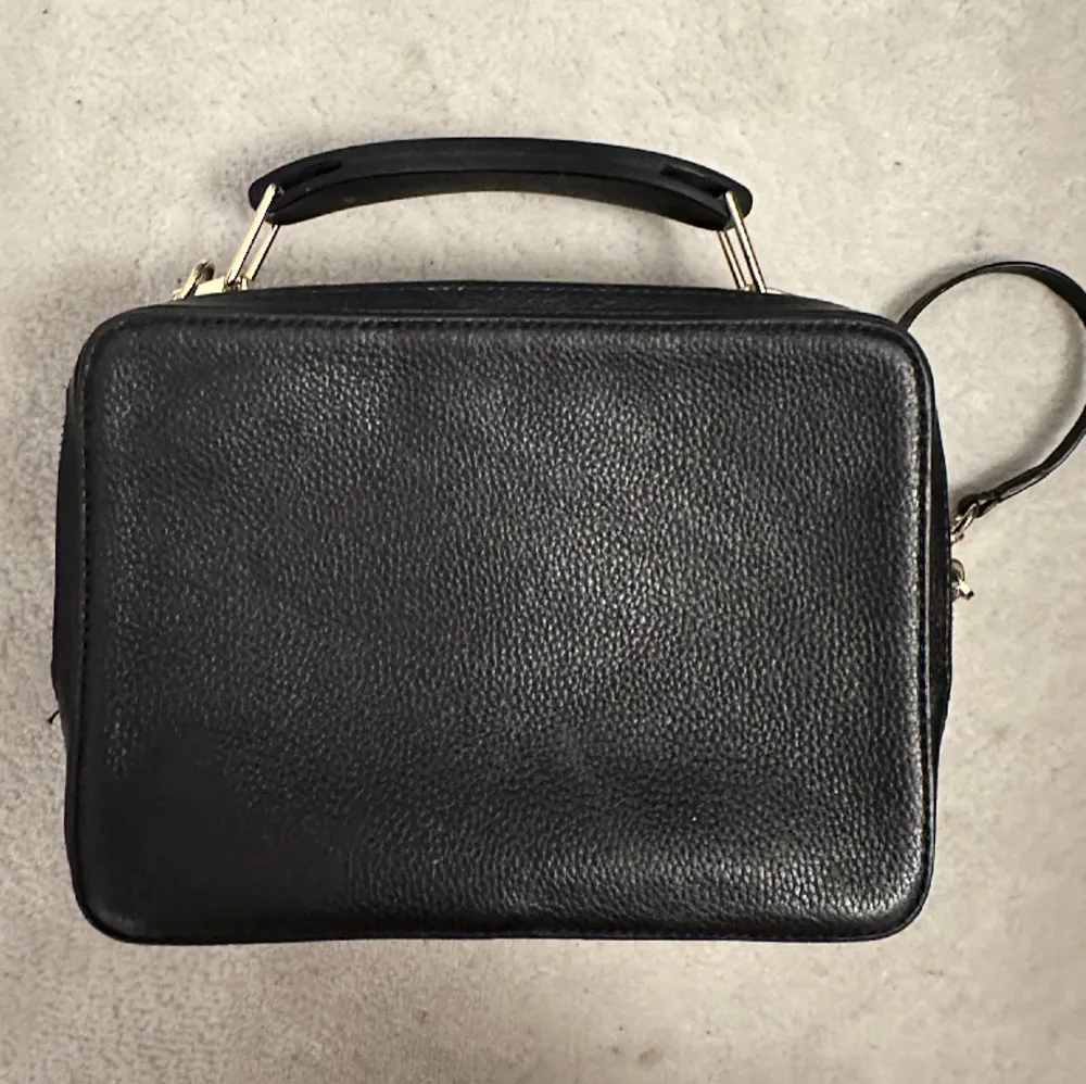 THE BOX 23 HAMMERED LEATHER BAG från Marc Jacobs i svart.  - äkta skinn - 17cm x 23cm x 8 cm - guldfärgade metalldetaljer   Väl använd, i gott skick utan några större skavanker, förutom att tyget iunti en av ”fickorna” av väskan är missfärgad. . Väskor.