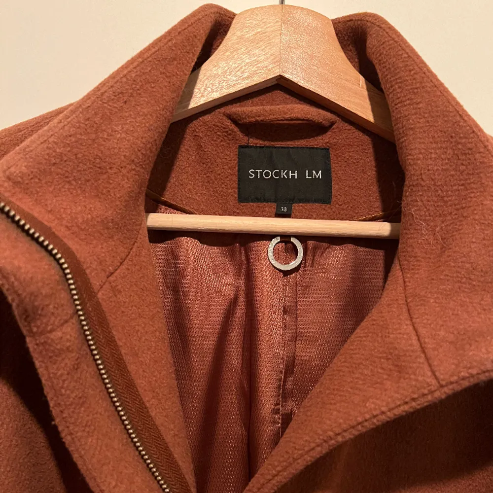 Rostbrun kappa från MQ av märket STOCKH LM. Storlek 38. Använd men i gott skick.   Yttertyg: 50 % Polyester, 50 % Ull Foder: 55 % Polyester, 45 % Viskos . Jackor.