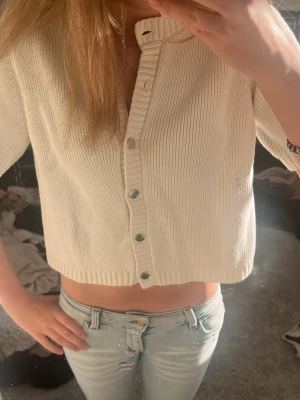 Vit  kofta från Gina Tricot - Kort, ribbad kofta i vit färg från Gina Tricot. Koftan har rund halsringning, knappar framtill och trekvartsärmar. Perfekt att styla med jeans eller kjol för en clean och enkel look.