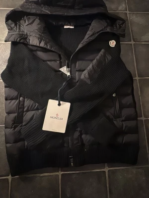 Svart dunväst med huva från Moncler - Snygg svart dunväst från Moncler med huva och stickade svarta ärmar. Helt ny inte använd någon gång, pris går att diskutera vid snabb affär 🚚💨