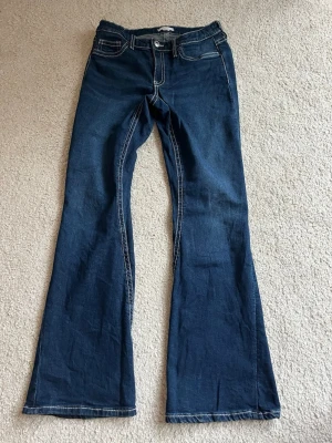 Mörkblå bootcut jeans Gina Tricot - Säljer ett par mörkblå bootcut jeans från Gina Tricot med kontrastsömmar och klassisk femficksmodell. Jeansen har normal midja och är tillverkade i ett mjukt denimtyg. Perfekta för en avslappnad men ändå trendig look.