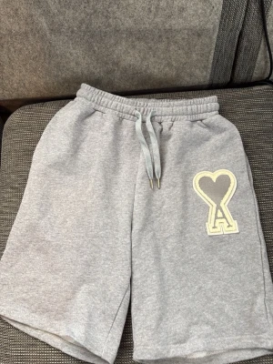 Grå shorts med hjärtlogga från Ami - Snygga grå shorts från Ami med elastisk midja och snörning. Mjukt bomullsmaterial och en stor broderad hjärtlogga framtill. Perfekta för en chill och avslappnad stil.