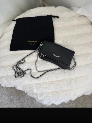 Zadig & Voltaire Rock Nano Axelremsväska Noir - Zadig & Voltaire Rock Nano Axelremsväska Noir Nypris: 2745kr. Pris kan diskuteras något. Sparsamt!!! Använd väldigt få gånger Finns en längre kedja och en kortare Höjd: 12cm Längd: 17cm Vidd: 3cm Handtag: 60cm Dustbag medföljer ej