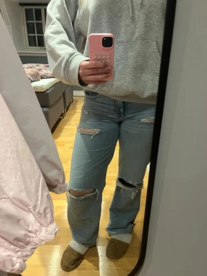 Ljusblå ripped jeans med raka ben - Säljer ett par ljusblå jeans med raka ben och flera slitningar vid knän och lår. Jeansen har klassisk femficksdesign och är tillverkade i denim. Perfekta för en avslappnad och trendig look.
