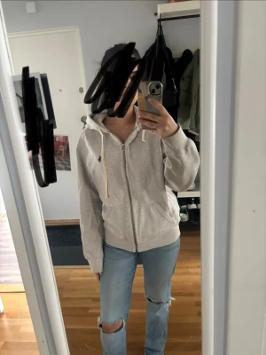 Beige ziphoodie med huva - Säljer en beige ziphoodie från Ralph Lauren med huva och dragsnören. Klassisk broderad logga på bröstet och två fickor framtill. Perfekt för en avslappnad och stilren look. Mjuk bomullsblandning som är skön att ha på sig.