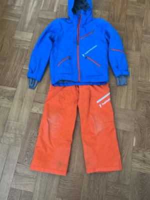 Orange täckbyxor från Peak Performance - Säljer ett par orange täckbyxor från Peak Performance med logga på vänster ben. Byxorna har en loose fit och är gjorda i slitstarkt material. Priset är för båda, går även att köpa separat.