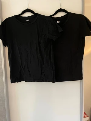 2 svarta T-shirts - Båda för 50kr. Två svarta basic t-shirts från 157 med rund halsringning och kort ärm. Perfekta att matcha med jeans eller shorts för en enkel och stilren look. Tillverkade i mjuk bomull.