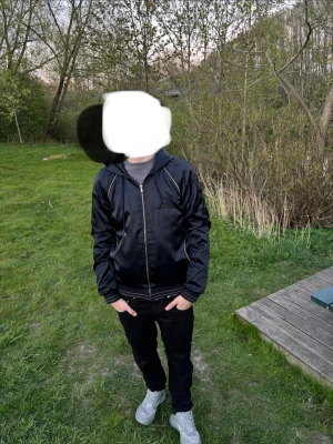 Dolce&gabbanaSvart bomberjacka med dragkedja - Stilren svart bomberjacka med klassisk dragkedja framtill och ribbade muddar vid ärmslut och midja. Jackan har en minimalistisk look och passar perfekt till streetwear-stilen. Materialet ser ut att vara glansigt, troligtvis polyester eller nylon.