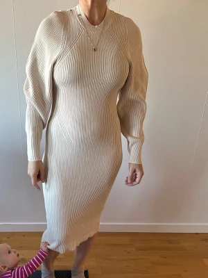 Beige ribbad långklänning - Snygg beige ribbad långklänning med lång ärm och rund halsringning. Klänningen har en figurnära passform och är tillverkad i ett stickat material som ger en mjuk och bekväm känsla. Perfekt för dig som gillar stilrena och trendiga plagg. Notera fläckarna, vi har inte försökt att tvätta den❗️