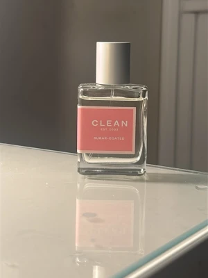 CLEAN Sugar-Coated parfym - Fräsch parfym från CLEAN med namnet Sugar-Coated. Flaskan är genomskinlig och fyrkantig med en rosa etikett och vit text. Locket är silverfärgat och flaskan är gjord av glas. Perfekt för dig som gillar söta och fräscha dofter. Nypris 540kr