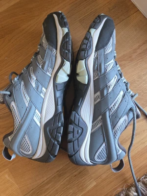 Grå sneakers med mesh och reflexdetaljer - Säljer ett par grå sneakers från Mountain Warehouse med coola meshpaneler för extra ventilation och reflexdetaljer. Skorna har kraftig sula, snörning och sportig look. Perfekta för dig som gillar streetstyle och bekväma skor.