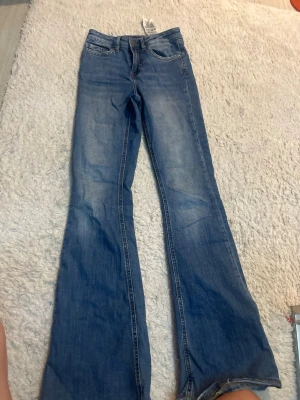 Blå bootcut jeans från LDM - Snygga blå bootcut jeans från New Yorker med klassisk femficksdesign och utsvängda ben. Jeansen har en lätt tvättad look och normal midja. Perfekta för dig som gillar retrostil och vill ha ett par jeans med lite extra attityd. Säljer för 250kr men original pris är 400kr