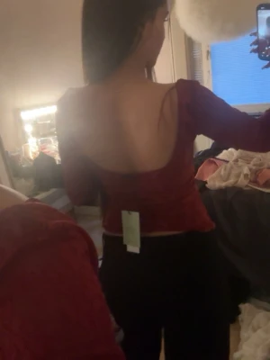 Röd långärmad topp med öppen rygg - Trendig röd topp med lång ärm och öppen rygg. Toppen har en söt rosettdetalj framtill och är croppad i modellen. Perfekt för dig som vill sticka ut med en snygg och ungdomlig stil.