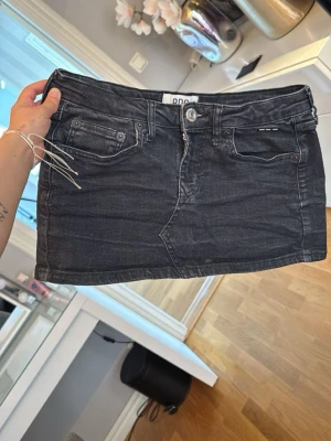 Svart jeanskjol från Dr. Denim - Snygg svart jeanskjol från Dr. Denim med klassisk femficksdesign och knapp- samt dragkedjestängning framtill. Kort modell med bälteshällor och en stilren look som passar till många outfits.