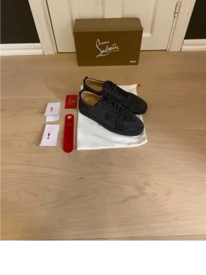 Mörkgrå sneakers från Louboutin - Snygga mörkgrå sneakers från Christian Louboutin i mocka med klassisk låg siluett. Skorna har rund tå, matchande skosnören och diskret logga på insidan. Perfekta för dig som gillar exklusiv och stilren design.