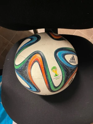 Adidas Brazuca fotboll VM 2014 - Säljer en Adidas Brazuca fotboll från VM 2014. Bollen är vit med färgglada mönster i blått, grönt, orange och svart. Tillverkad i slitstarkt syntetmaterial och har officiell FIFA World Cup-logga tryckt på sidan.