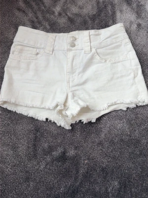 Vita jeansshorts - Säljer ett par vita medel hög midjade jeansshorts med råa kanter och klassiska femficksdetaljer. Shortsen har dubbla knappar framtill och bälteshällor. Perfekta för varma dagar och en avslappnad look. Säljer pågrund av att det inte är min stil längre.  Nackdel, blir lätt smutsiga. 