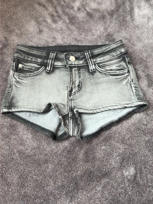 Grå mini denimshorts med rå kant - Säljer ett par gråa mini denimshorts från Cheap Monday med rå kant nertill och klassisk femficksdesign. Shortsen har knappgylf och en rosa Cheap Monday-logga bak. Perfekta för sommaren och ger en cool, avslappnad vibe. Säljer pågrund av att det inte passar mig. 
