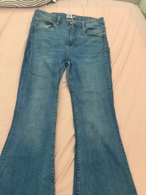 Blå utsvängda jeans  - Säljer ett par blå jeans från H&M med utsvängda ben och klassisk femficksmodell. Jeansen har normalhög midja och är gjorda i denim med lätt tvättad look. Perfekta för dig som gillar retrostil och vill ha ett par snygga och bekväma jeans.