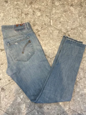 Dondup George Jeans - Säljer ett par ljusblå skinny jeans med slitningar och råa benslut. Jeansen har klassisk femficksdesign och dragkedja i bakfickan som detalj. Perfekta för en avslappnad och trendig look. Dondup George jenas som är skit snygga i storlek 34 vilket motsvarar 31 eller 32 på slim jeans. Nypris 3000 och är i 8,5/10 skick