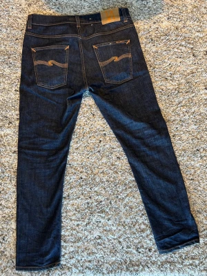 Mörkblå jeans från Nudie - Snygga mörkblå skinny jeans från Nudie med klassiska orange sömmar och broderade bakfickor.