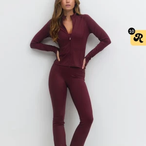 Vinrött loungewear-set med dragkedja - Snyggt vinrött loungewear-set med långärmad topp och dragkedja framtill samt matchande tights. Setet har en figurnära passform och är gjort i ett mjukt, stretchigt material som känns skönt mot huden. Perfekt för chill eller hemmadagar.